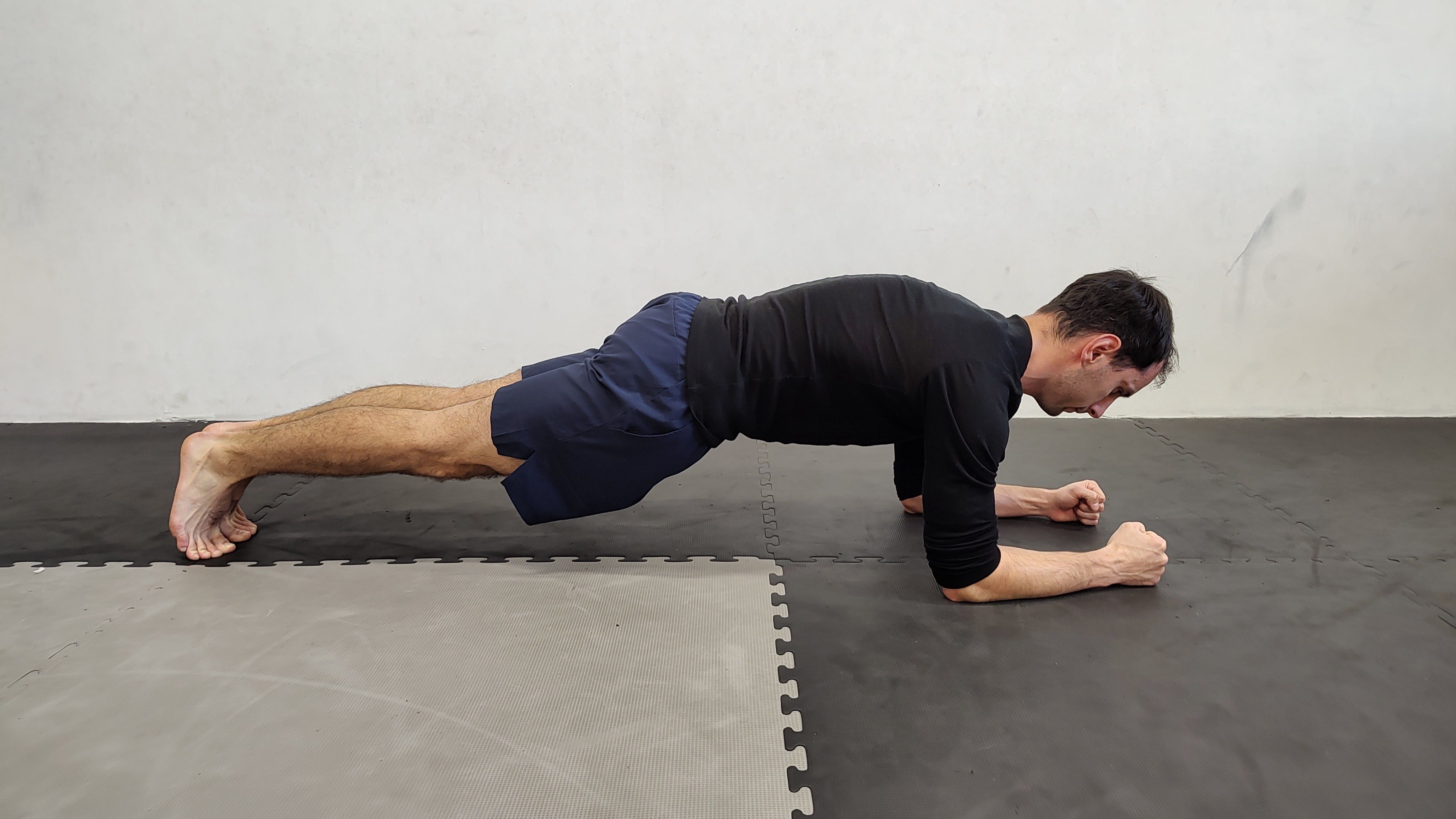 Muž v tělocvičně cvičí plank na loktech.